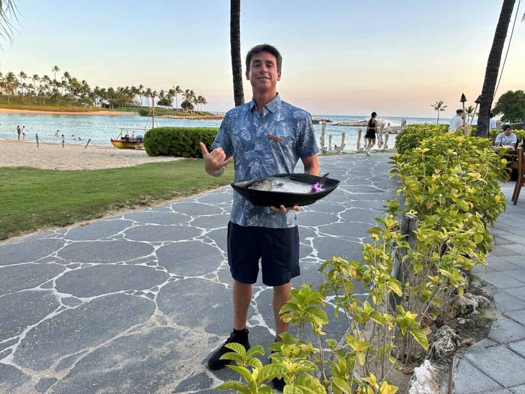 Restaurant staff member holding a whole fish near the beach at Mina’s Fish House.