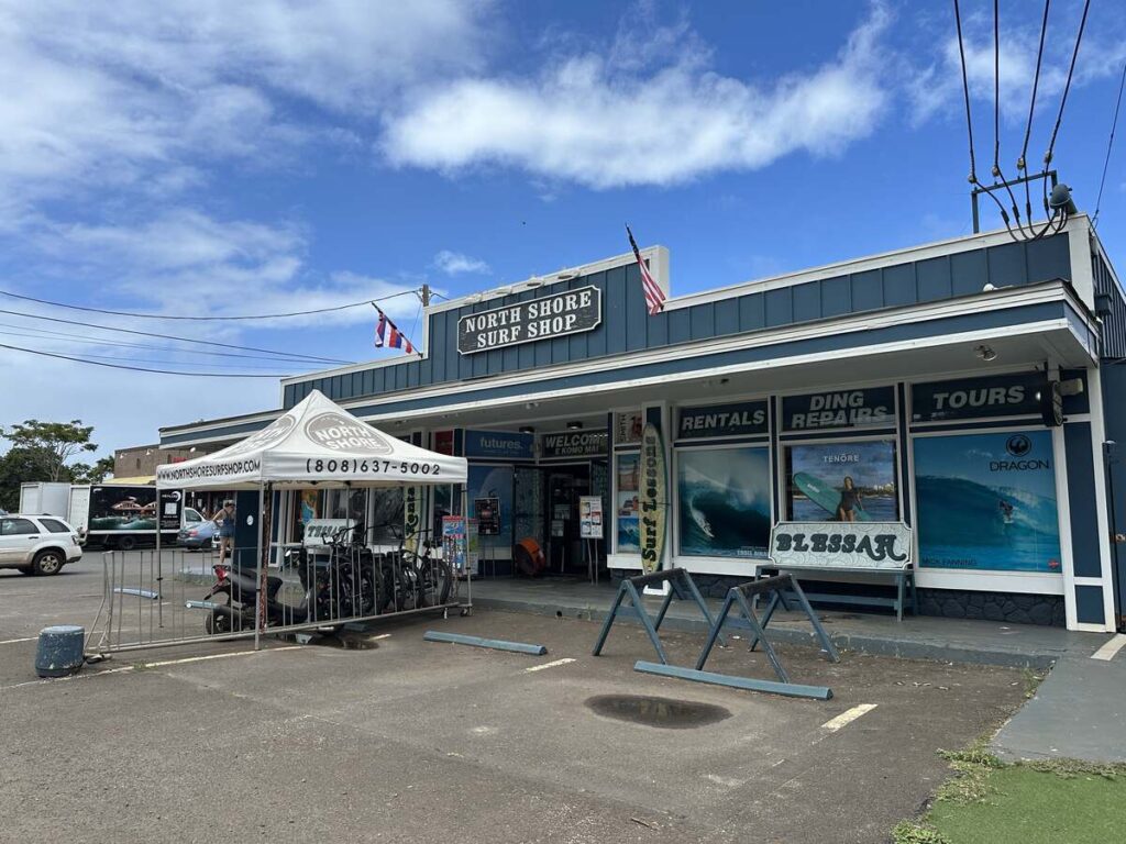 Exterior of North Shore Surf Shop with surfboard rentals, ding repair signs, and a blue sky above Haleʻiwa.