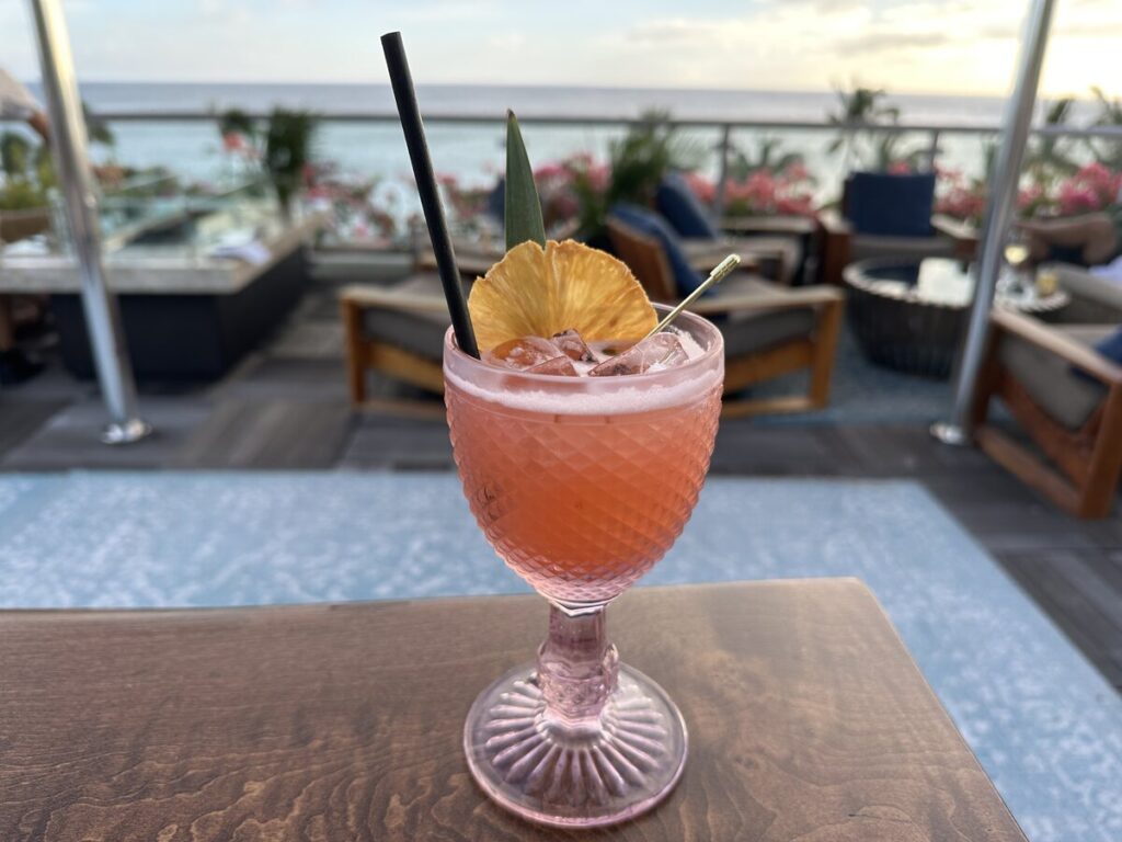 Pink cocktail in a textured glass at five | one | six with ocean views in the background.