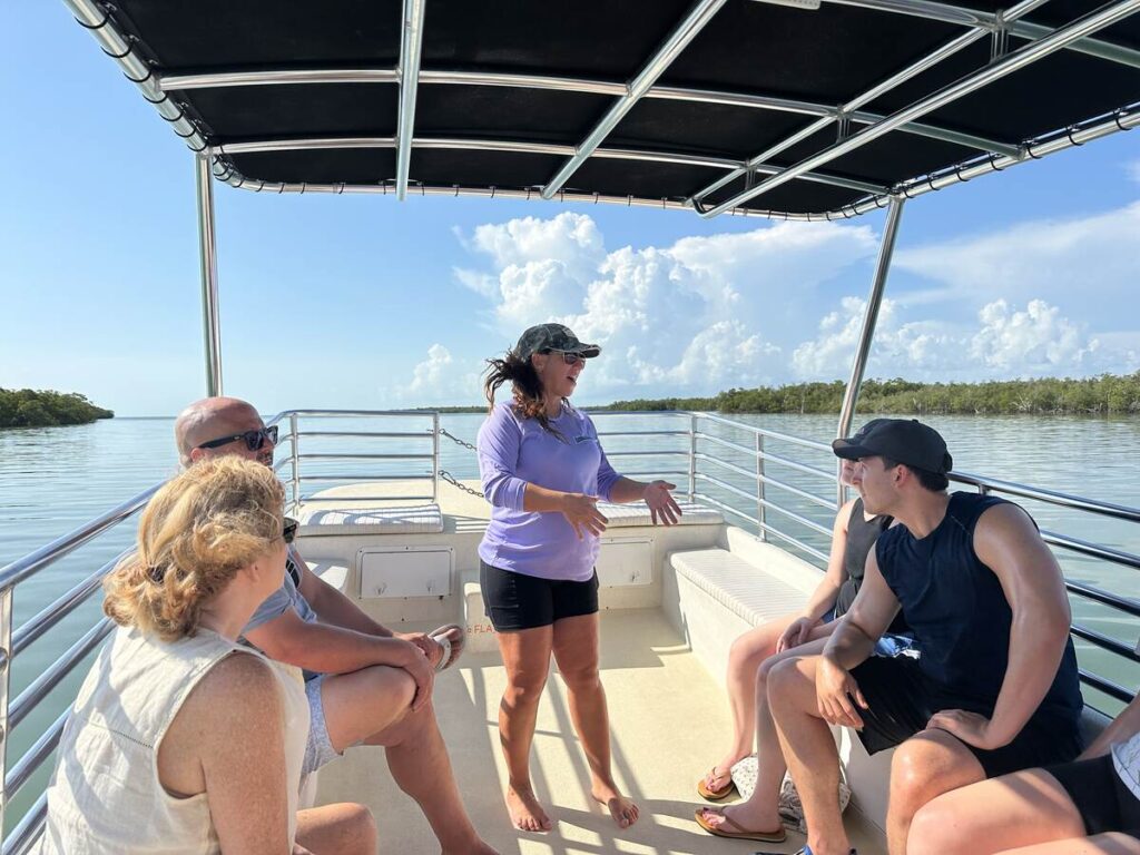 A Florida eco tour guide speaks to passengers on a boat surrounded by calm water, mangroves, and bright summer clouds.