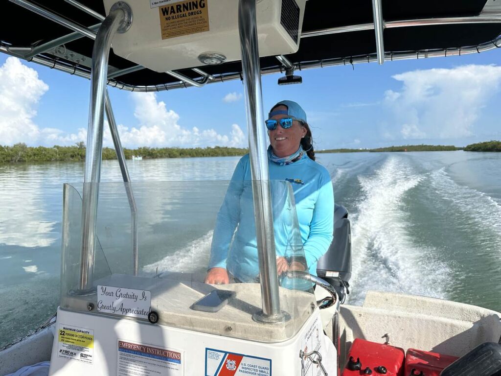 A boat captain smiles at the helm during a Ten Thousand Islands eco tour, with the boat’s wake trailing behind.