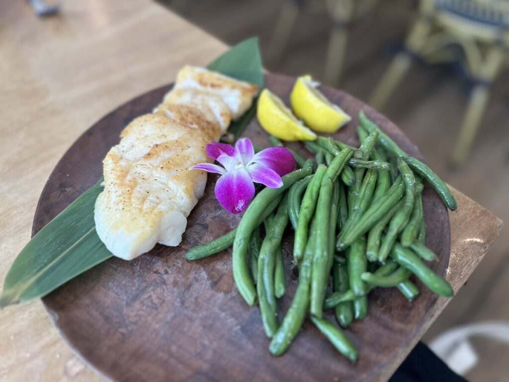 Grilled white fish served with green beans, lemon wedges, and an orchid garnish on a wooden plate in Marco Island.