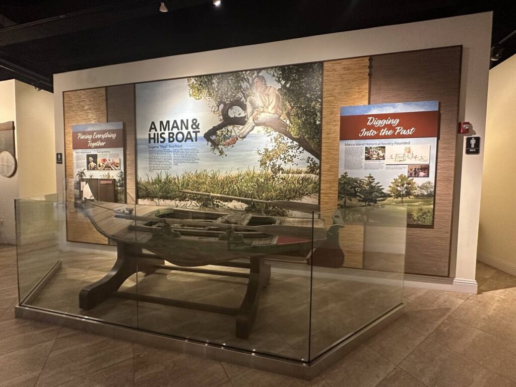 Marco Island Historical Museum exhibit titled “A Man & His Boat,” with a small wooden boat displayed behind glass.