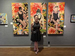 Executive director standing in front of three vivid tropical mixed-media artworks at Marco Island Center for the Arts.