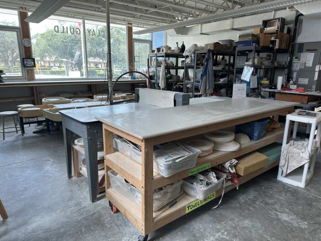 Clay studio with pottery wheels, worktables, shelves, tools, and bags of studio supplies.