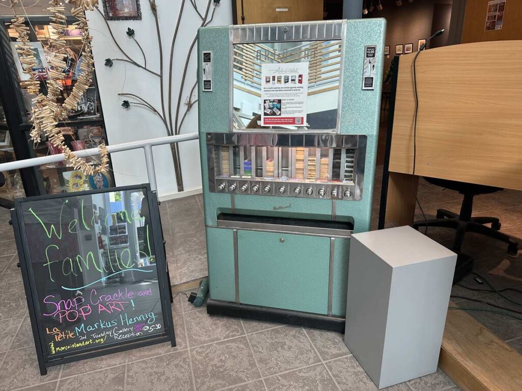Retro aqua vending machine beside a welcome sign promoting pop art at the arts centre.