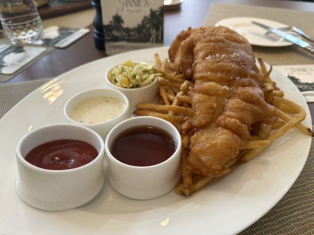 A fish-and-chips style dish served at Annie’s Bistro in Naples, with fries, coleslaw, and three dipping sauces on a white plate.