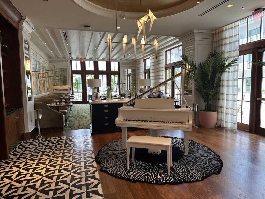The elegant dining room at Annie’s Bistro in Naples, featuring a white grand piano, patterned flooring, large windows, and soft coastal décor.