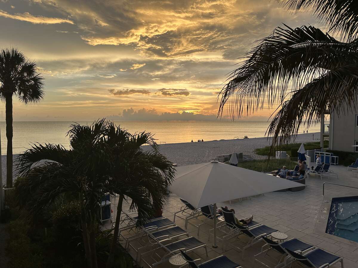 Sunset view from Edgewater Beach Hotel in Naples, with palm trees, pool loungers, beach, and the Gulf of Mexico.