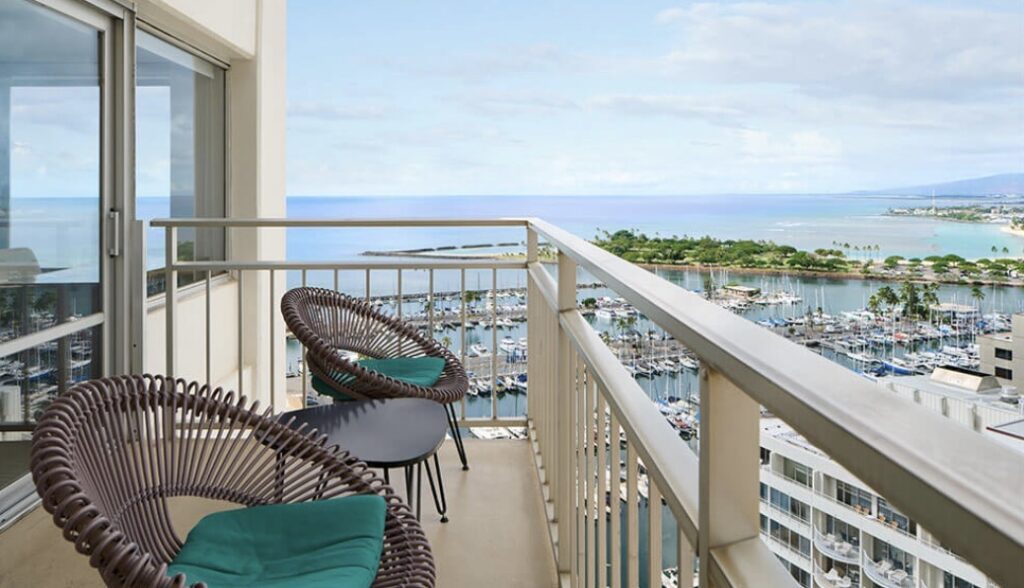 Balcony with two chairs overlooking the marina, ocean, and coastline near Waikīkī.
