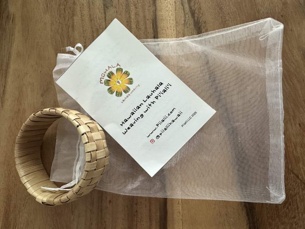 Handwoven lauhala bracelet on a wooden table with a workshop card from Four Seasons Resort Oahu.