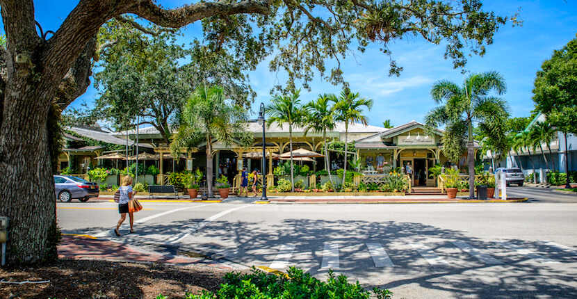 Third Street South shopping district in Naples, Florida, with palm trees, storefronts, outdoor seating, and pedestrians on a sunny street.