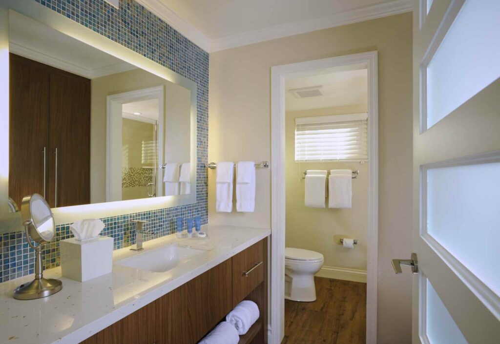 Bathroom inside a suite at Edgewater Beach Hotel, with a large mirror, blue tile accent wall, white countertop, towels, and separate toilet area.
