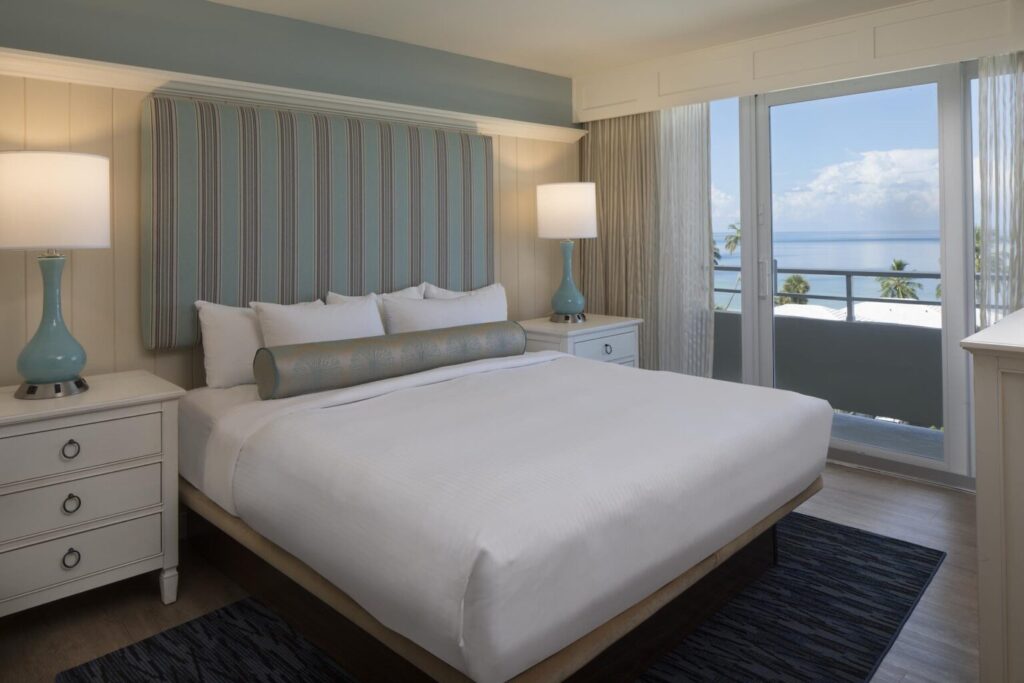 King bedroom at Edgewater Beach Hotel in Naples, with coastal blue décor, white bedding, and a balcony view of the Gulf of Mexico.