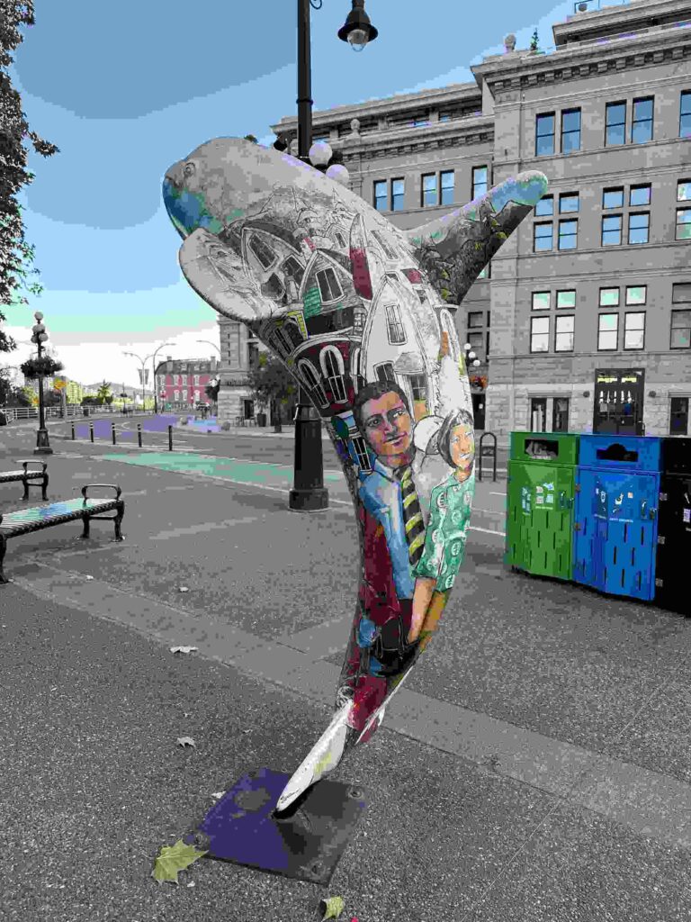 Painted orca public art sculpture on a downtown Victoria sidewalk.