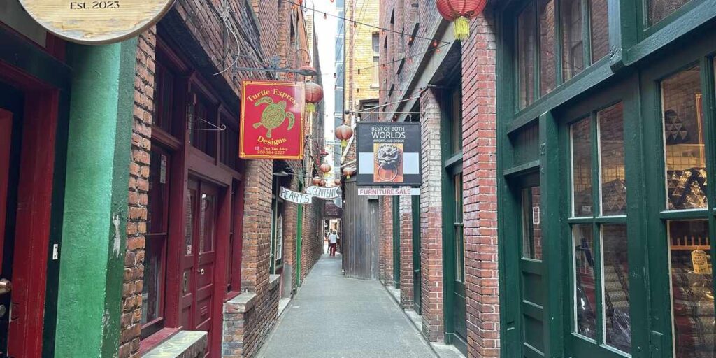 Narrow brick-lined Fan Tan Alley with shops and hanging lanterns in Victoria’s Chinatown.